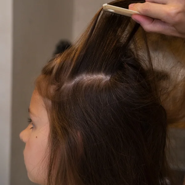 Une petite fille reçoit une coupe de cheveux chez le coiffeur, assise sur une chaise avec un tablier.