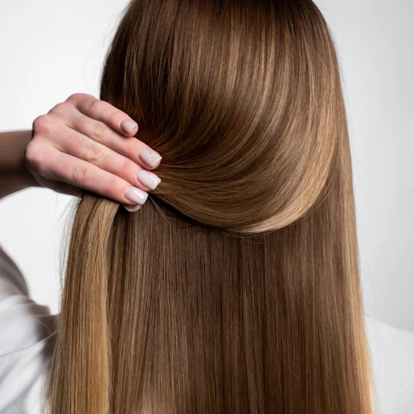 A woman with long straight hair is gently combing her hair with a brush.