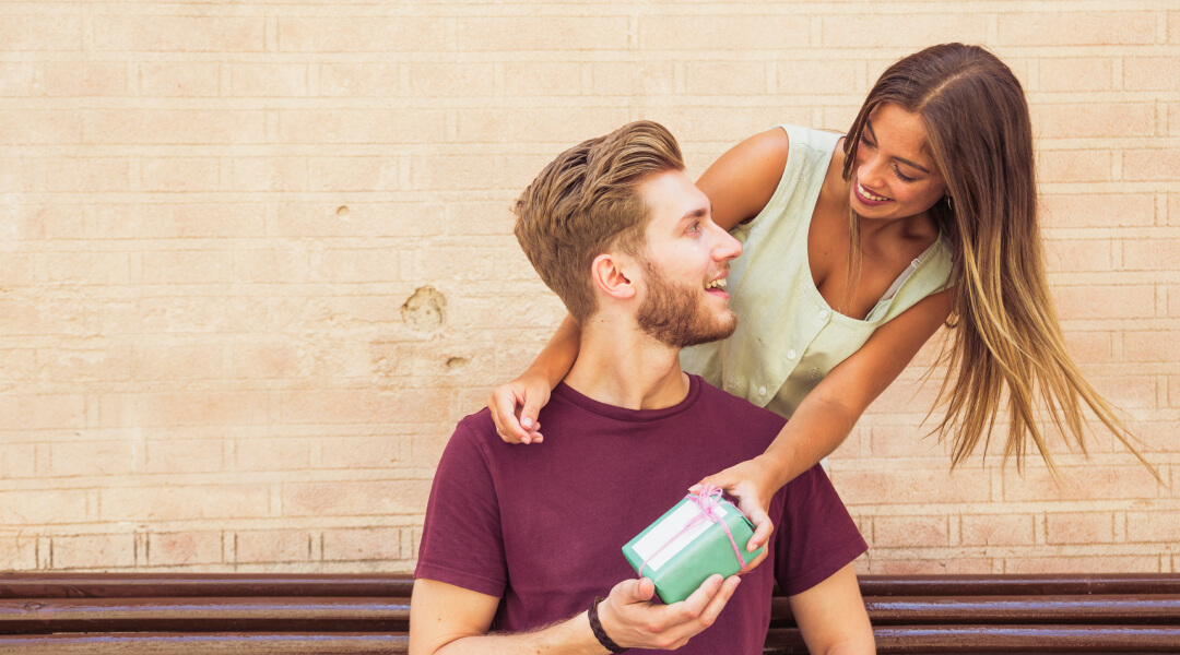 Un homme offre un cadeau à une femme sur un banc, symbolisant des soins capillaires pour la Saint-Valentin.