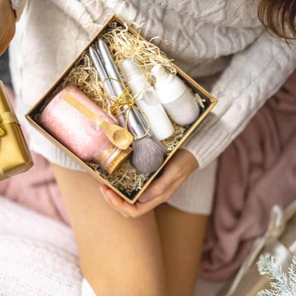 A woman holds a box filled with cosmetics and hair products, ideal gifts for Valentine's Day.