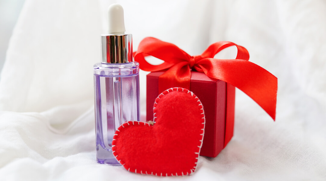A bottle of perfume beside a red heart, symbolizing Valentine's Day gift ideas for hair care for him and her.